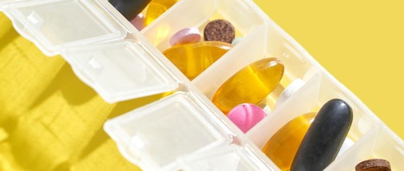 Weekly pill organiser with supplements and vitamins on yellow background.